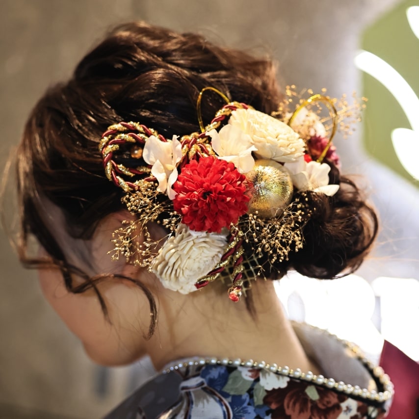 緩く巻いたヘアをざっくり編み込んでフェミニンに。花、水引、組紐のバランスが絶妙な髪飾りがアクセント。