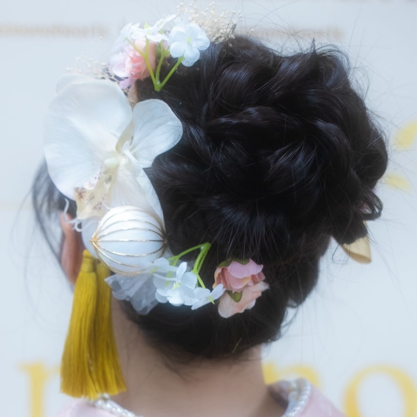 髪をツイストさせてピンで留めたまとめ髪。弧を描くように胡蝶蘭などの造花とタッセルを飾り華やかに。