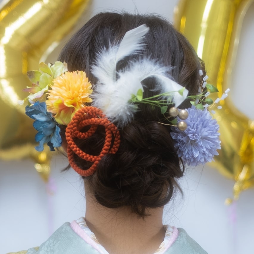 大人っぽいシニヨンに優しい色味の花々をカラフルに飾って。ふんわりとした羽でさらに柔らかい雰囲気に。