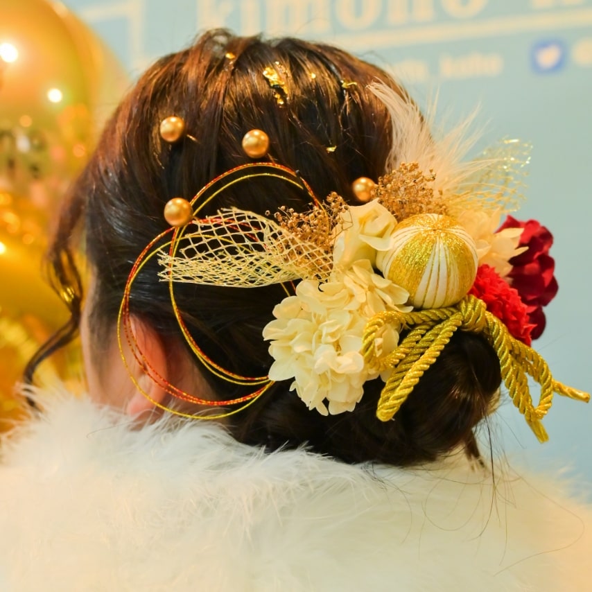 ローシニヨンに花や水引、手毬風の飾りをあしらって。パールのヘアピンでさらにキュートな印象に。