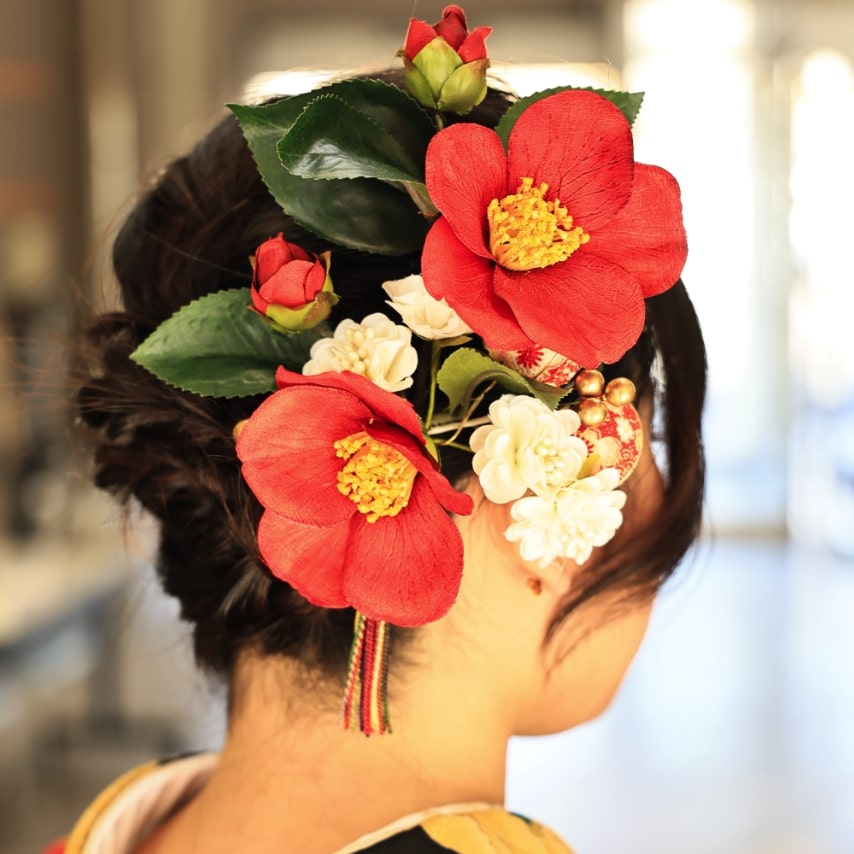 編み込みできっちりまとめ上げたヘアアレンジに、大きな生花風の椿の髪飾りが際立ちます。可憐でハイカラなオトナスタイル。
